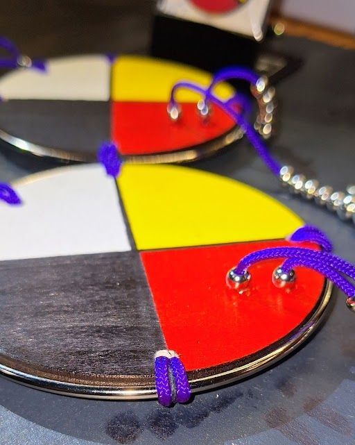 Native American pendants with a four-color wheel design, blue string, and beaded accents on a tan surface.