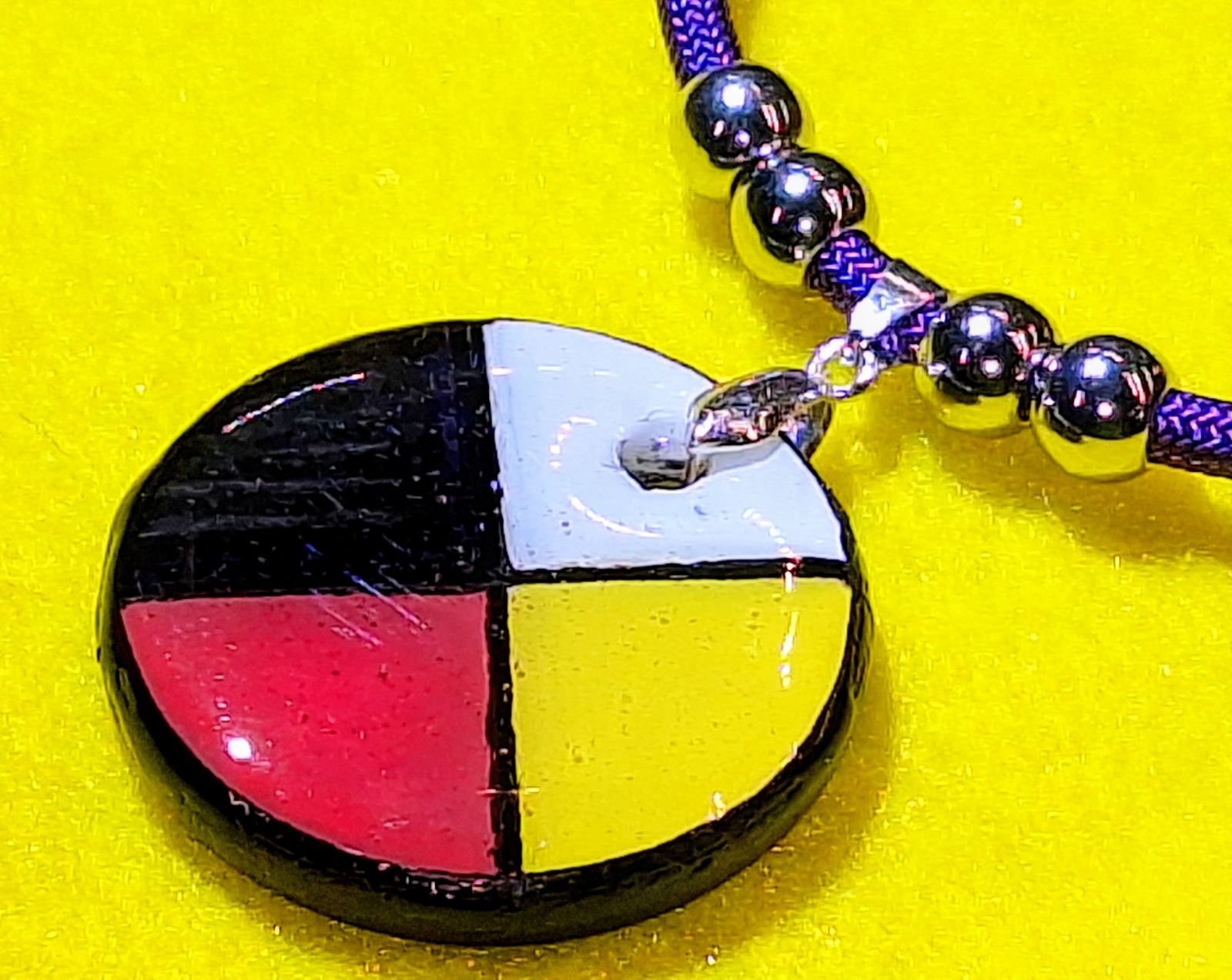 A circular pendant with quadrants of black, white, red, and yellow, on a purple beaded necklace.