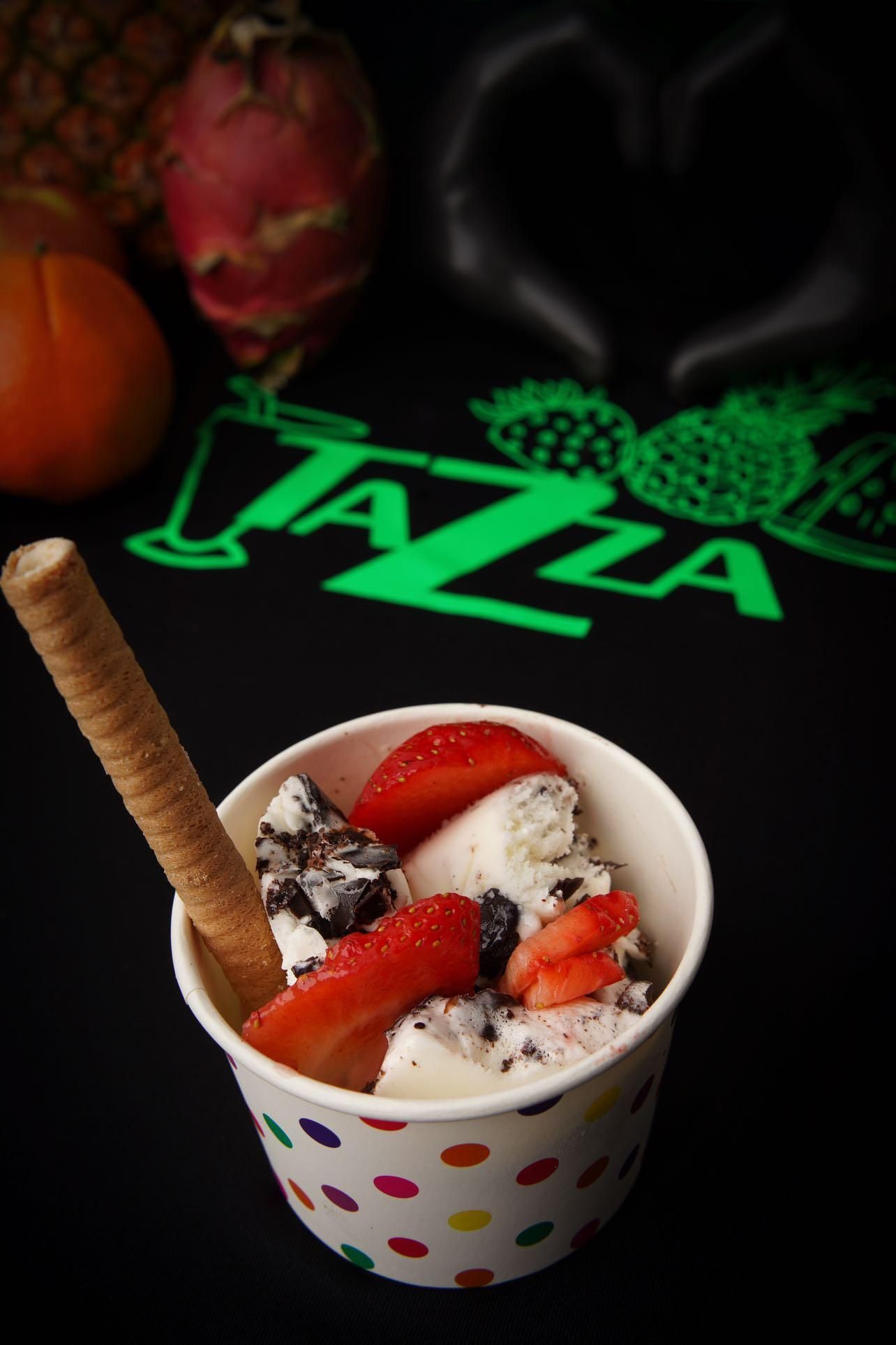 A cup of ice cream with strawberries and wafer sticks on a table.