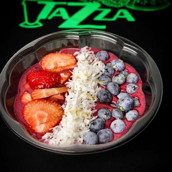 A bowl of strawberries blueberries and coconut on a table in front of a sign that says tazza