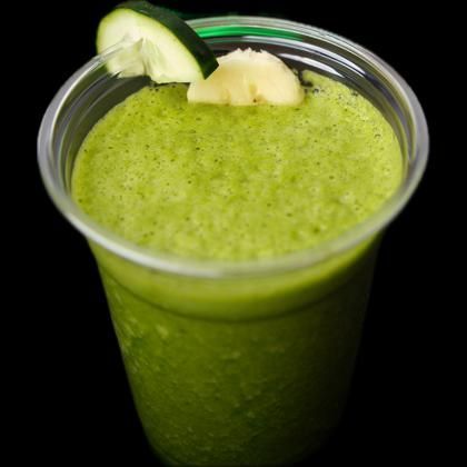 A green smoothie in a plastic cup with a cucumber slice on top
