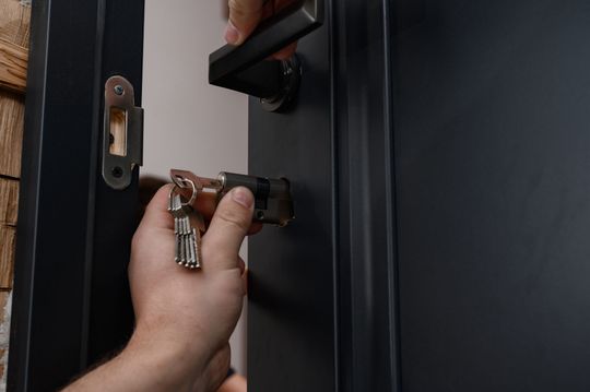 Hand unlocking a black front door with a key in the lock