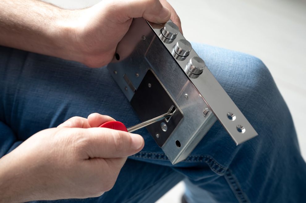 Hands using a screwdriver to adjust a metal lock on a blue-jean-clad lap