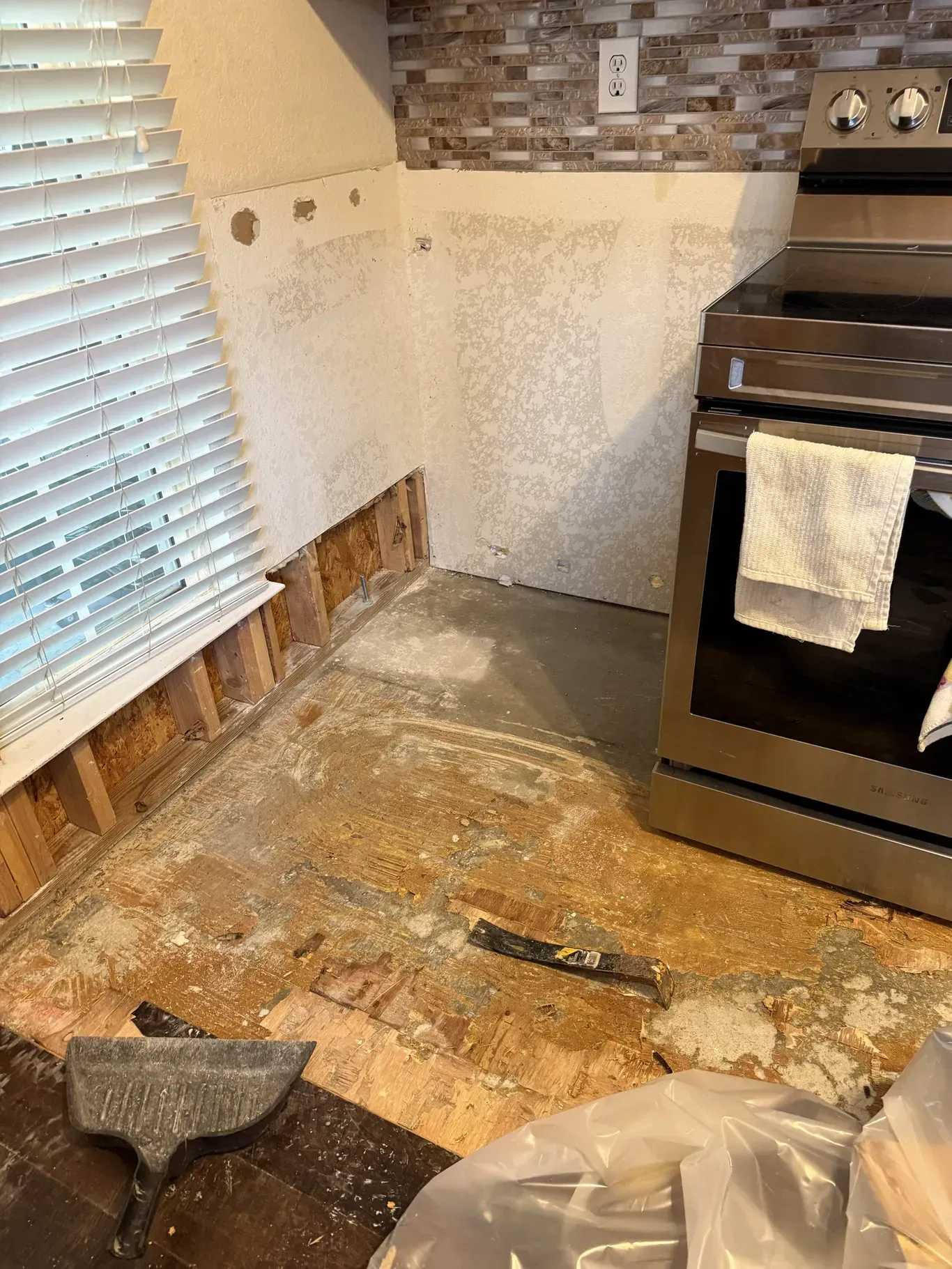 Kitchen renovation in progress: exposed wall studs, flooring debris, and a stainless steel oven.