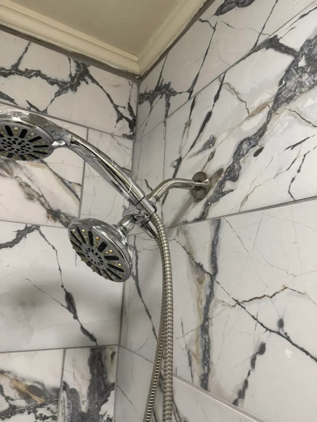 Chrome dual showerhead against white and gray marble tile.