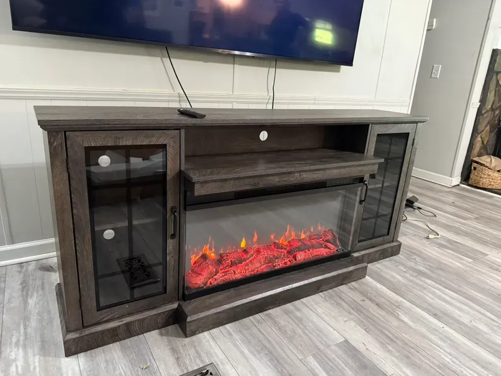 A gray TV stand with a built-in electric fireplace and glass-fronted cabinets. A TV is mounted above it.