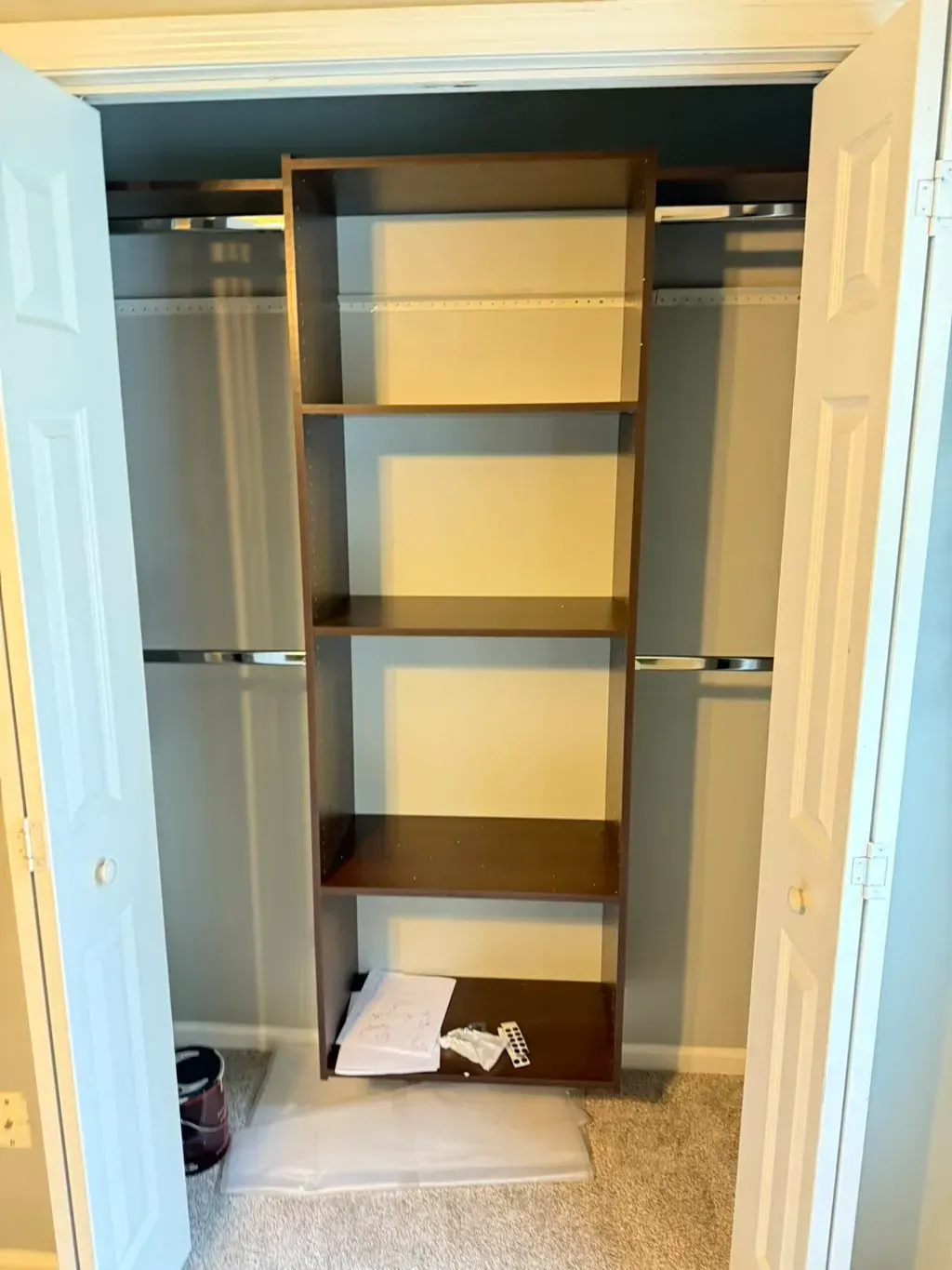 Brown shelf unit inside a closet, between closed white doors, on carpet.