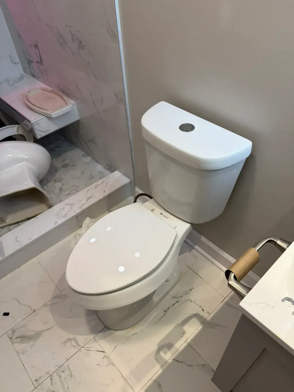 White toilet in a bathroom with marble flooring and a wall-mounted tank.