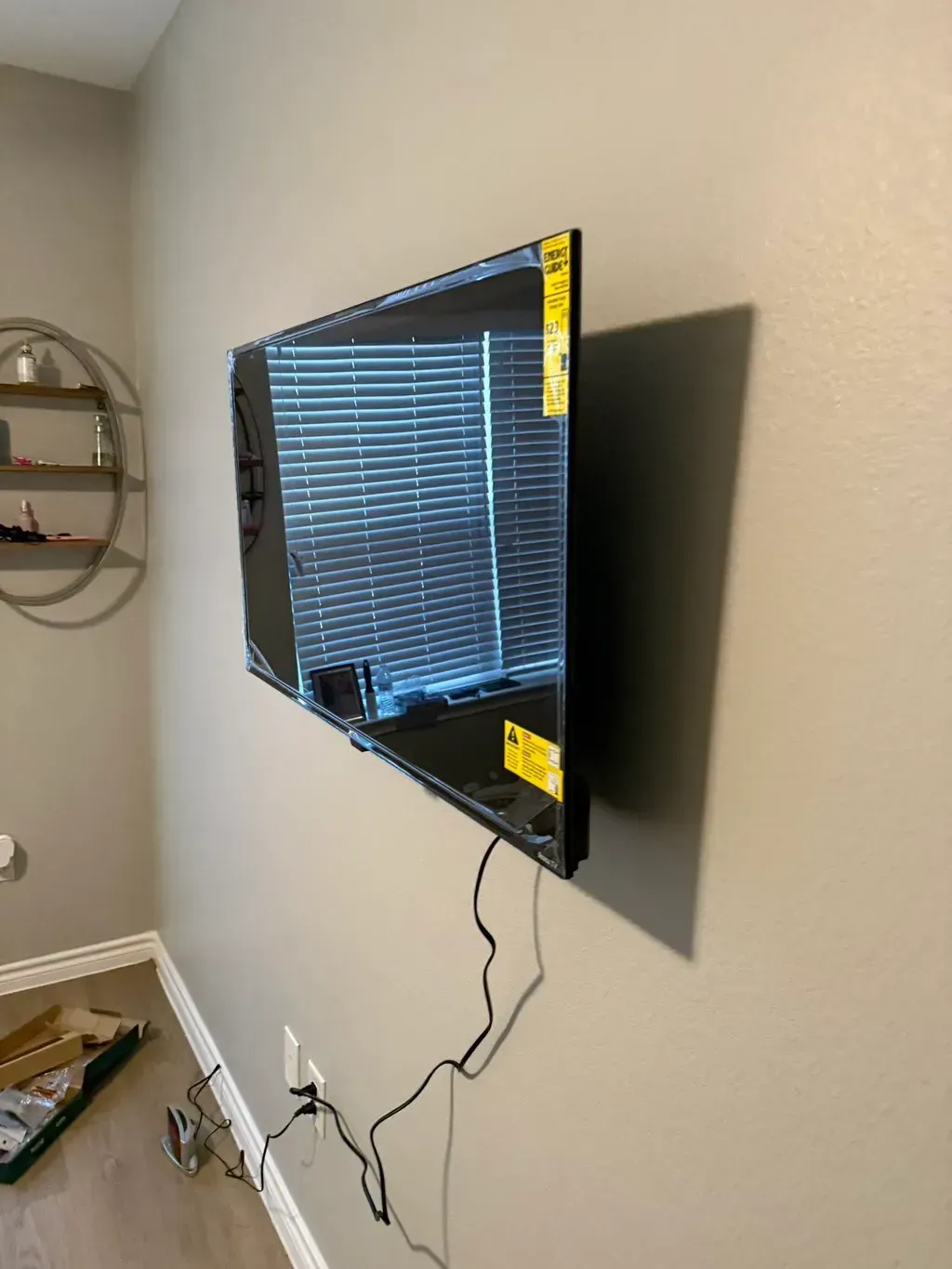 A flat-screen TV mounted on a gray wall with power cords dangling below.