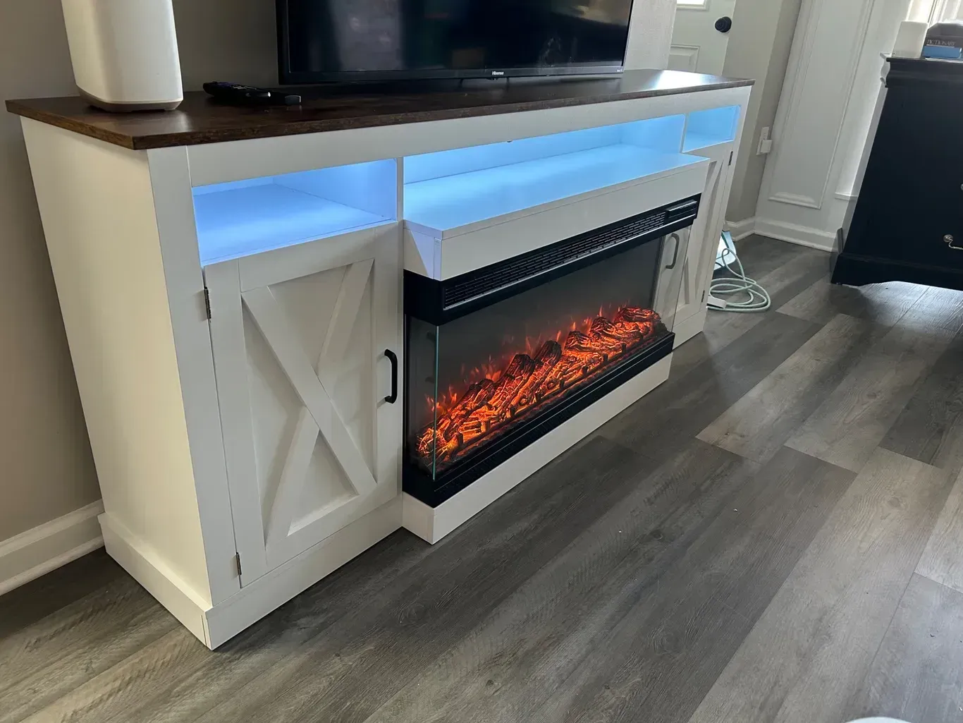 White TV stand with electric fireplace, blue light, and dark wood top.