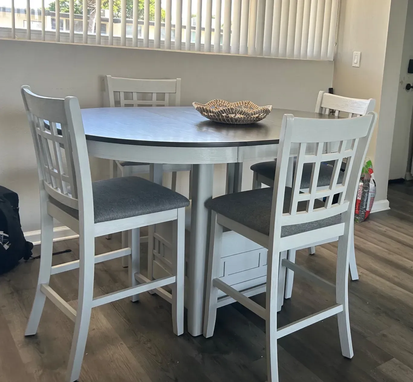 A round dining table with four white chairs with gray seats in a home setting.