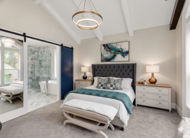 Bedroom with blue sliding door to bathroom, king bed with tufted headboard, art, and chandelier.