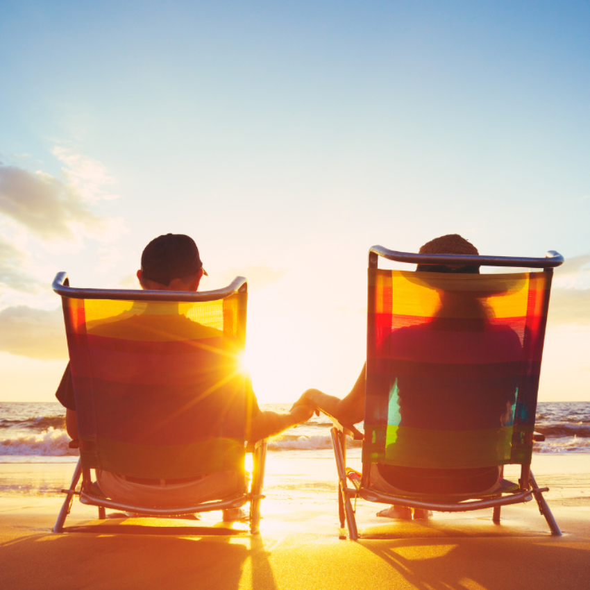 Two people in beach chairs, holding hands, watching sunset over the ocean.