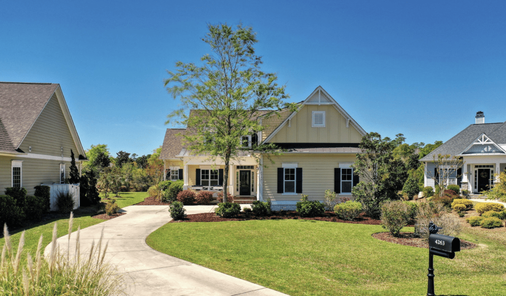 Yellow house with black shutters, a curving driveway, and manicured lawn under a blue sky.