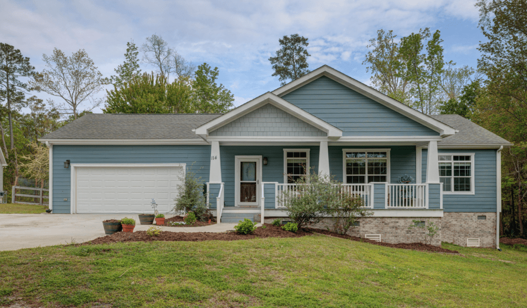Blue house with white trim and a two-car garage sits on a grassy lawn.