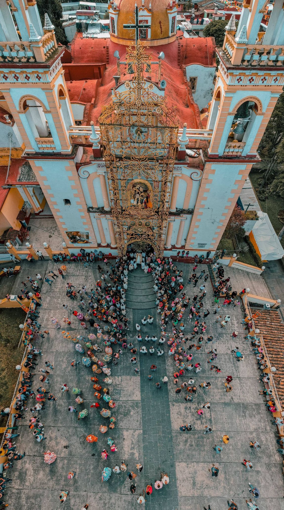 Procesión multitudinaria frente a una iglesia ornamentada con fachadas blancas y naranjas