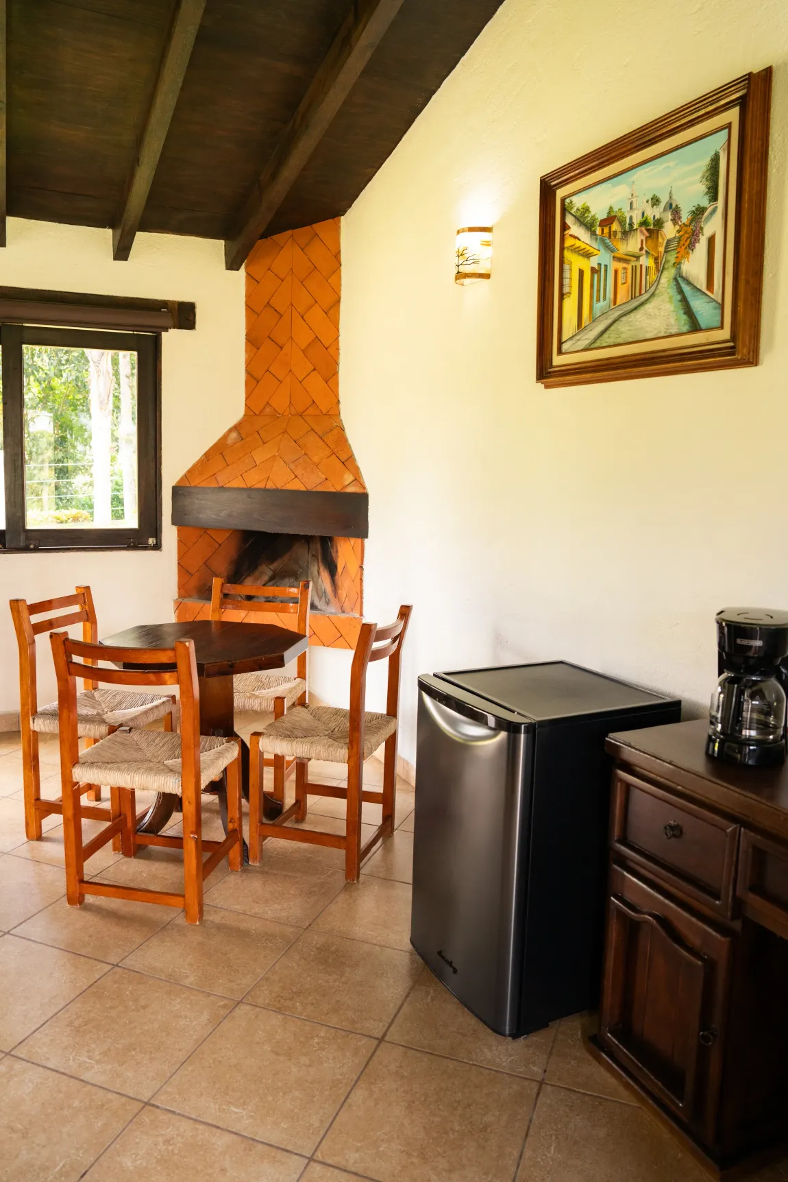 Acogedor comedor rústico con mesa de madera, chimenea, mininevera y cuadros enmarcados.
