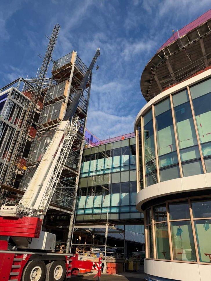 Construction site with a crane beside a curved glass building under a blue sky