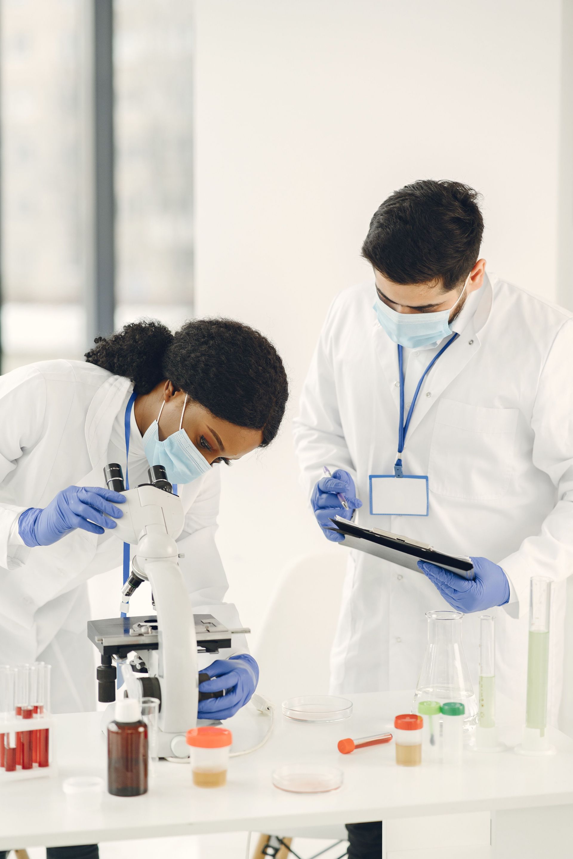 Lab technicians in white coats examining test tubes and a tablet in a laboratory