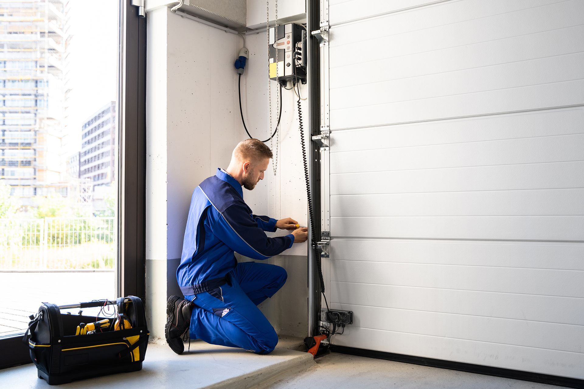 A man is kneeling down in a garage working on a garage door.