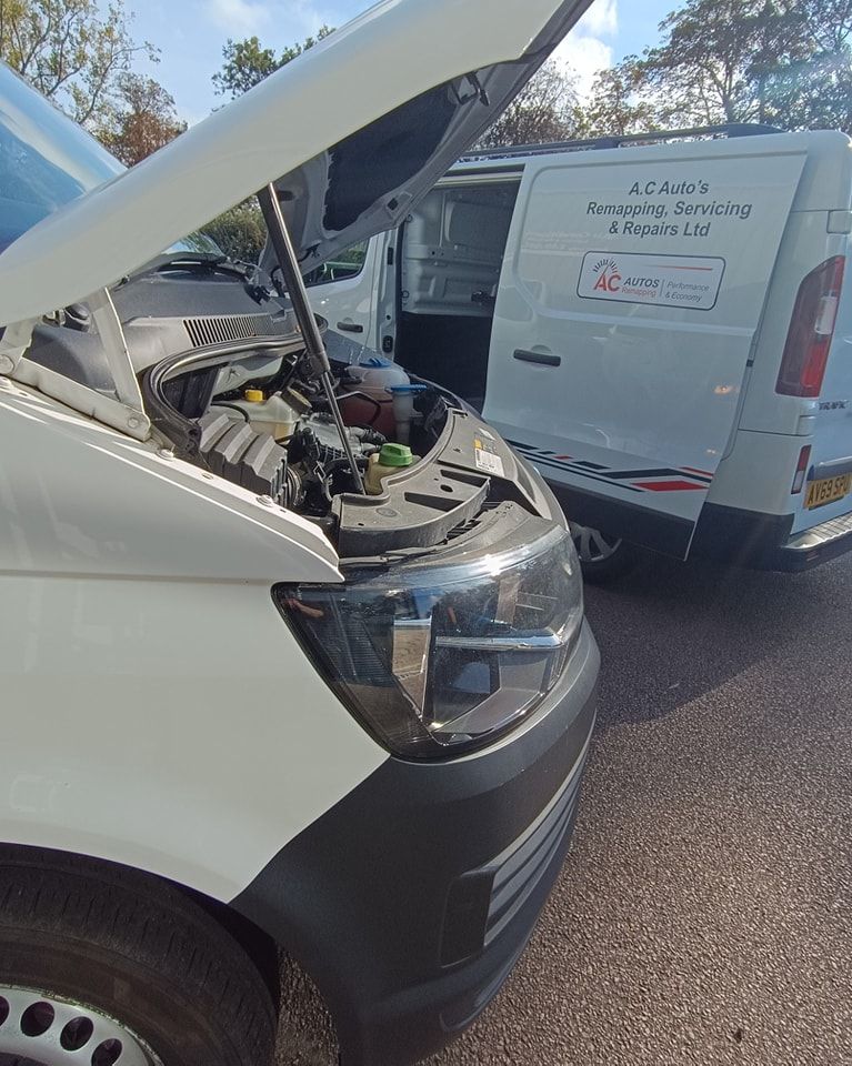 A white van with its hood open is parked next to another van.