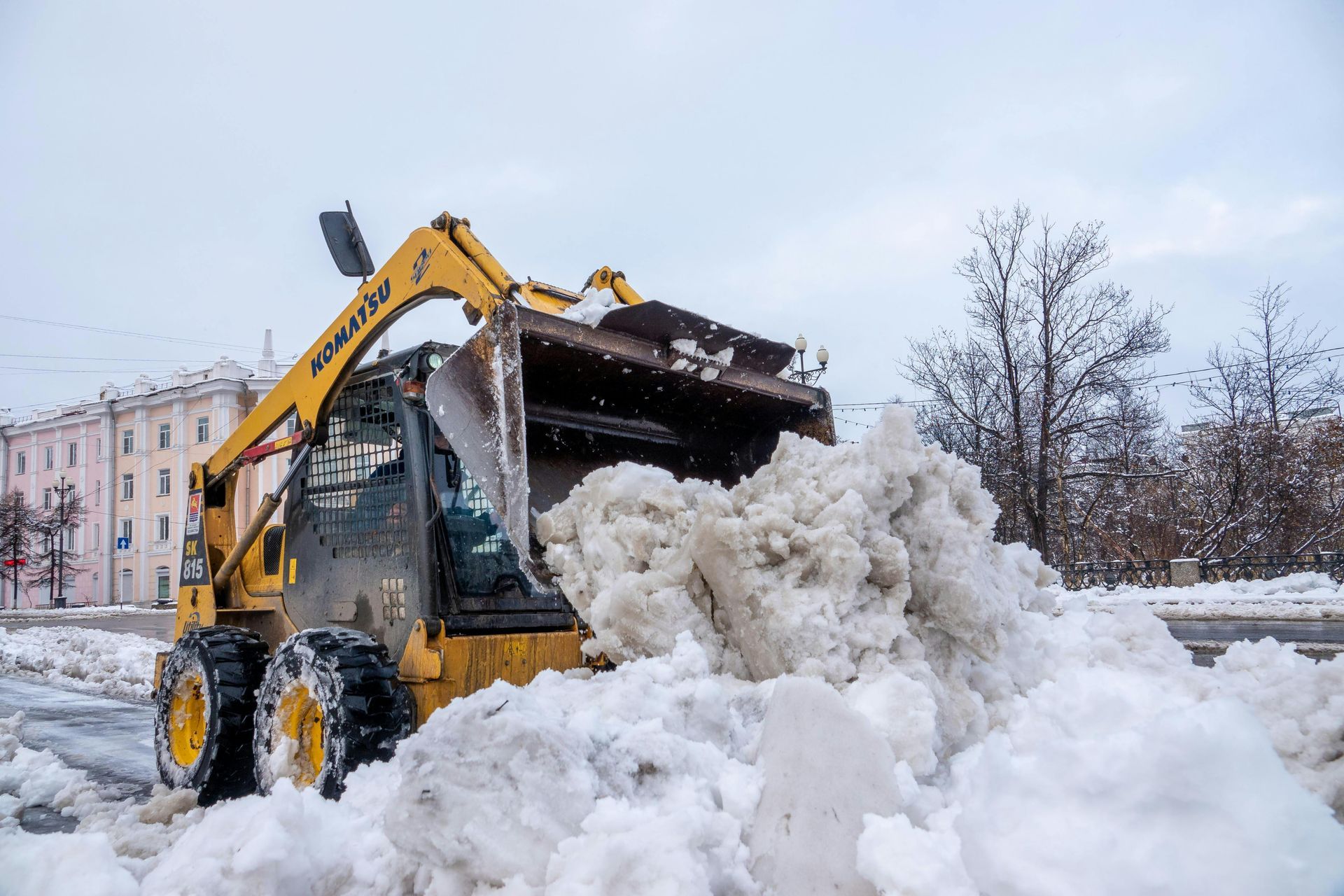 Yellow backhoe clearing a large snow pile on a city street in winter