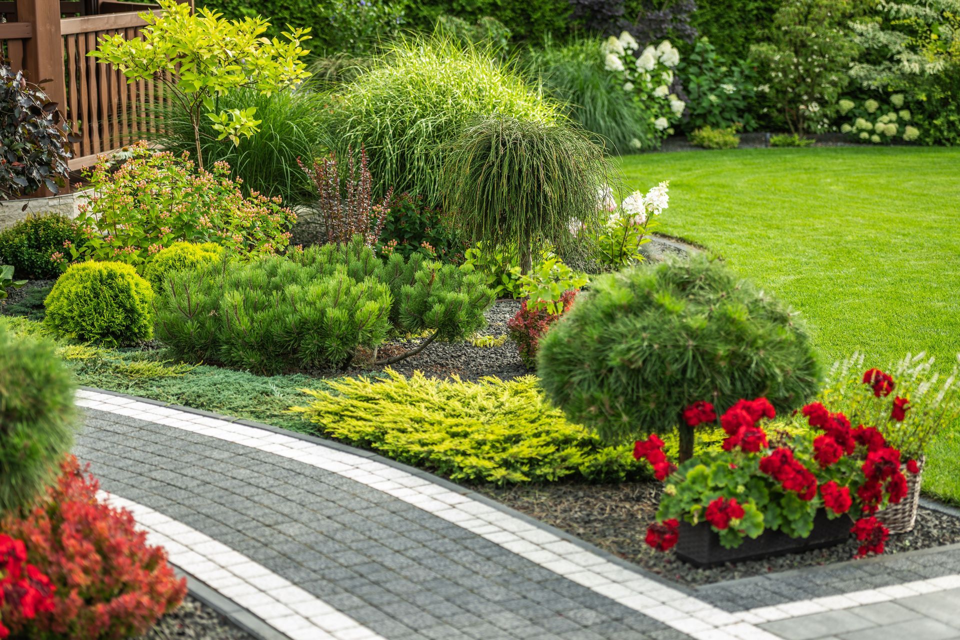Lush landscaped garden with curved stone path, green shrubs, and bright red flowers.