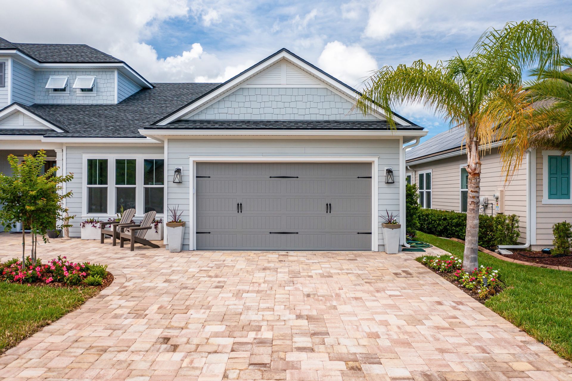 Suburban house with a two-car garage, stone driveway, and palm trees in front of a clear blue sky.