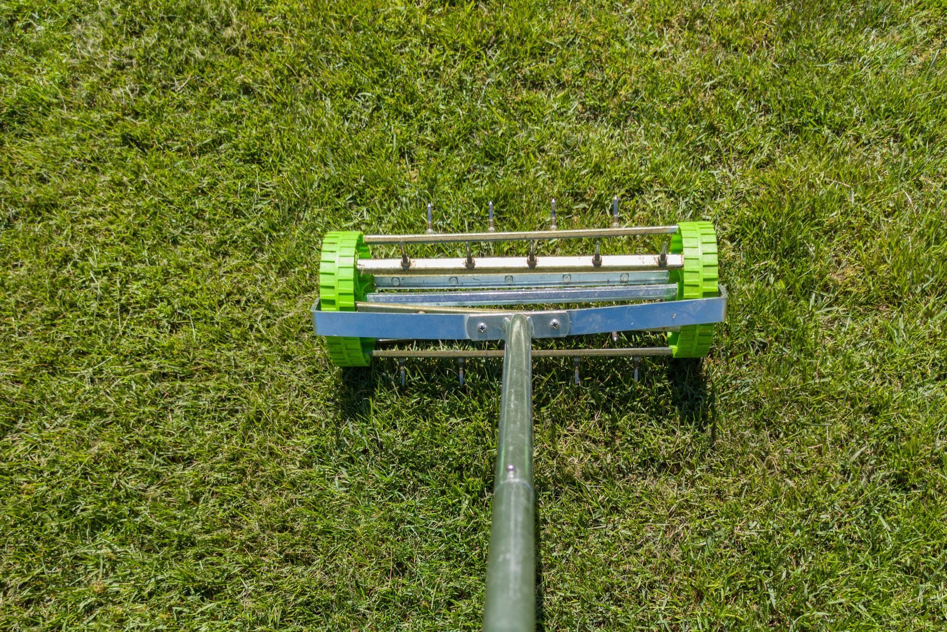 Lawn mower cutting green grass, viewed from above with the handle in the foreground