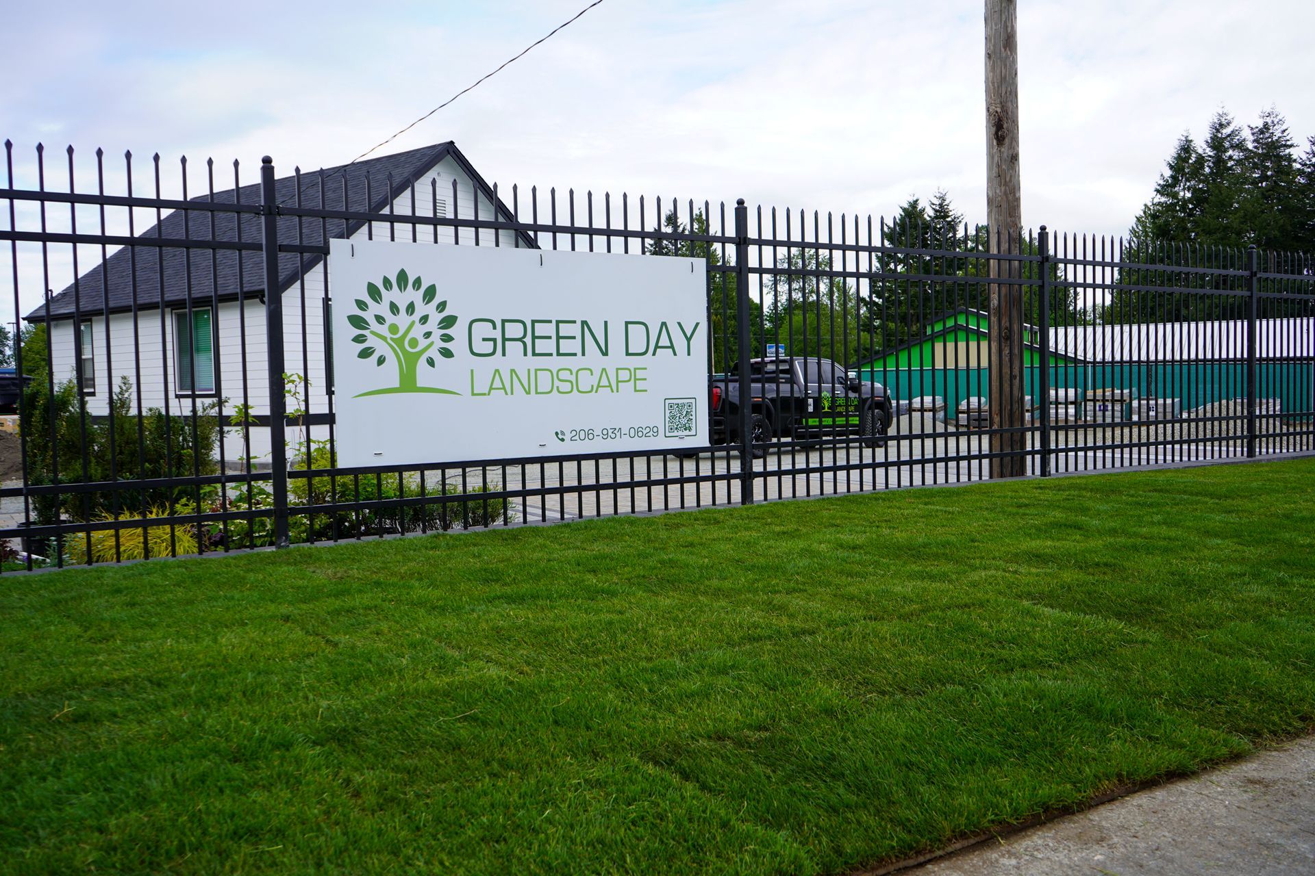 Green Day Landscape sign behind black fence; green grass in the foreground.