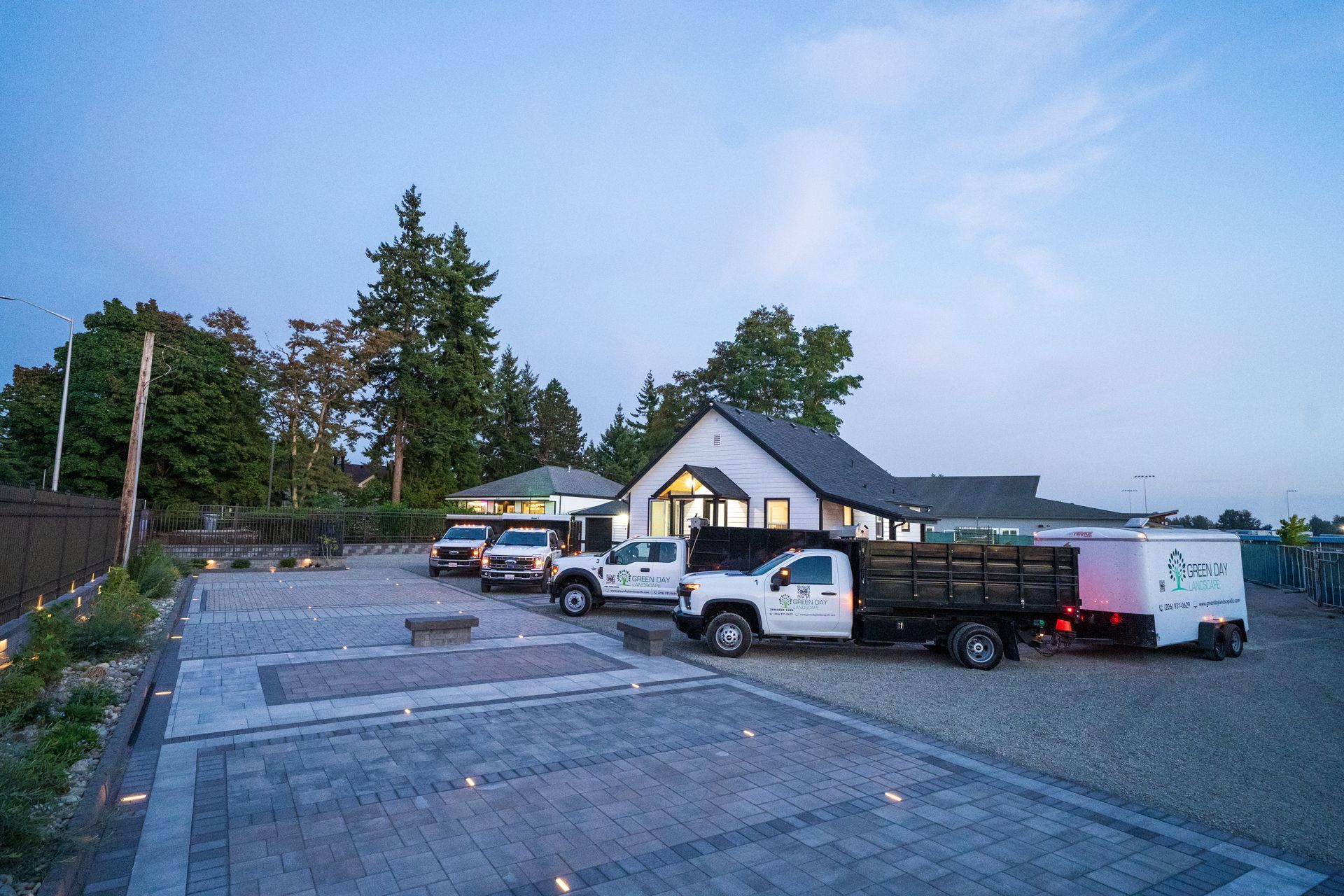 Landscaping company vehicles parked in front of a building at dusk.