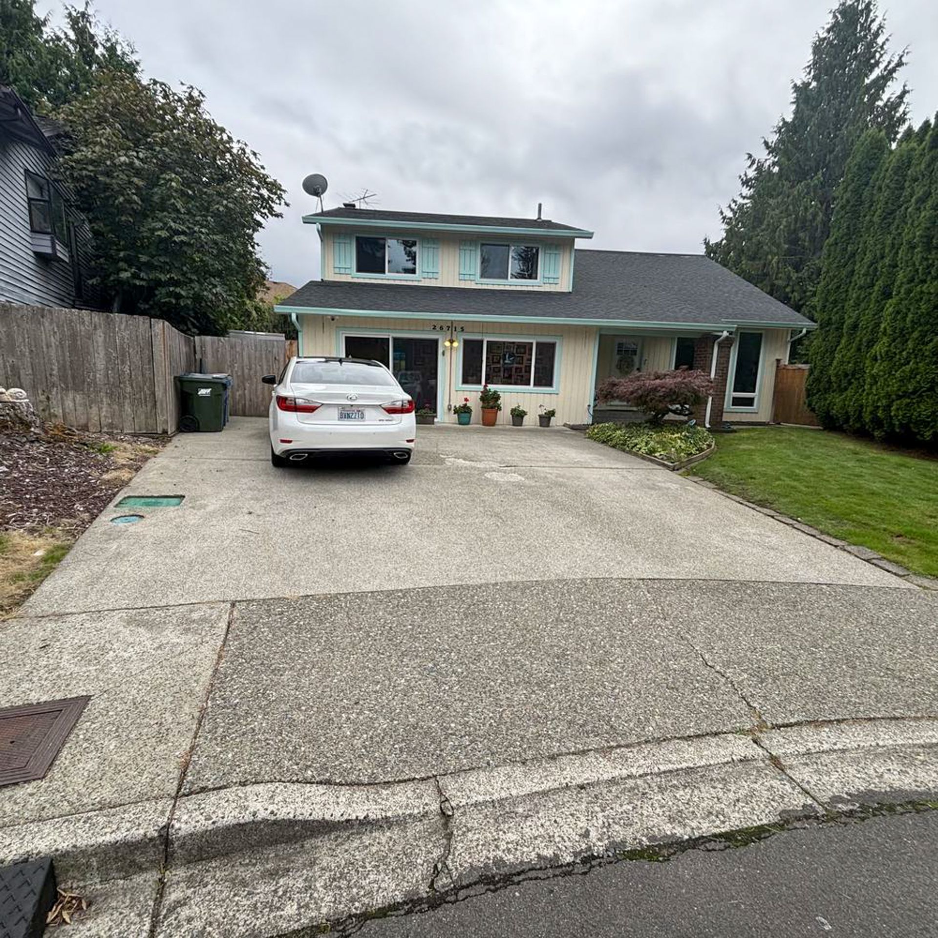 A two-story light yellow house with a car parked in the driveway on a cloudy day.