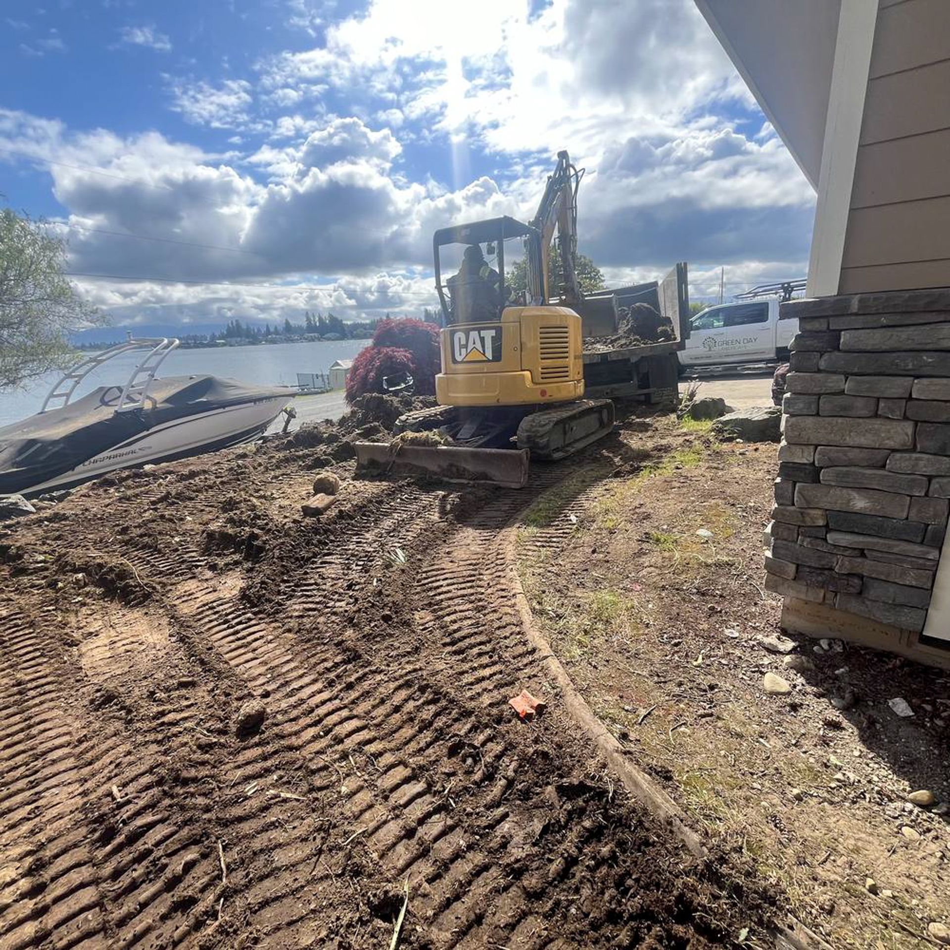 Yellow CAT excavator on muddy ground near water, loading a dump truck on a sunny day.