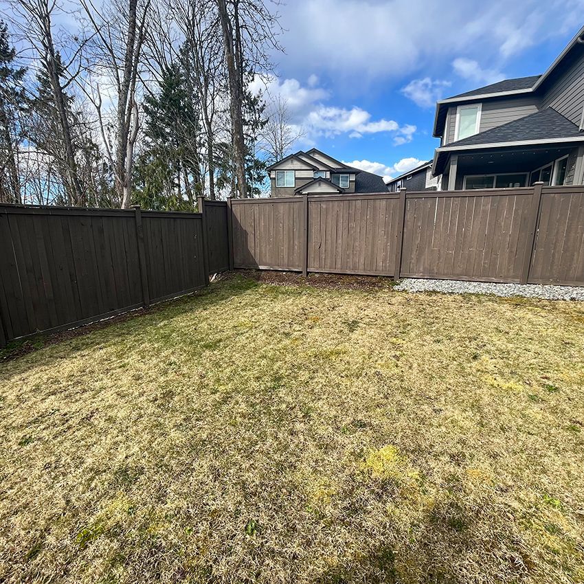 A backyard with brown fence, dry grass, and a cloudy sky. Houses are visible in the background.