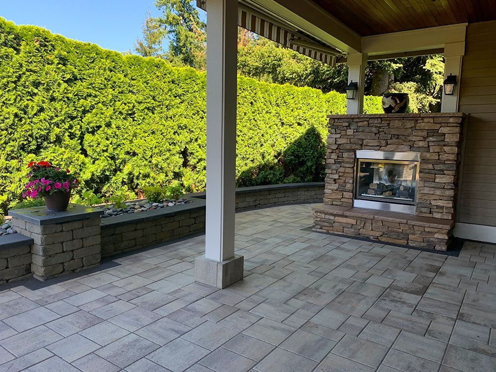Patio with stone fireplace, landscaping, and paved floor under a covered porch.