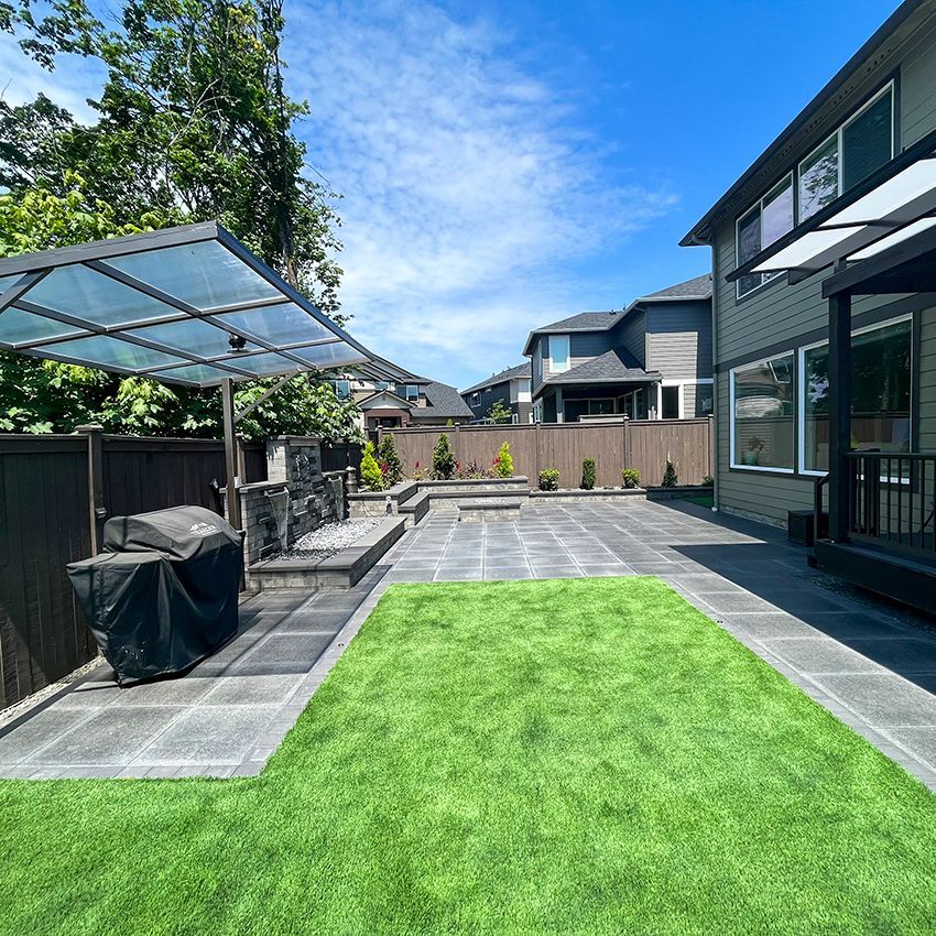 Backyard patio with BBQ, artificial turf, and house. Sunny day.