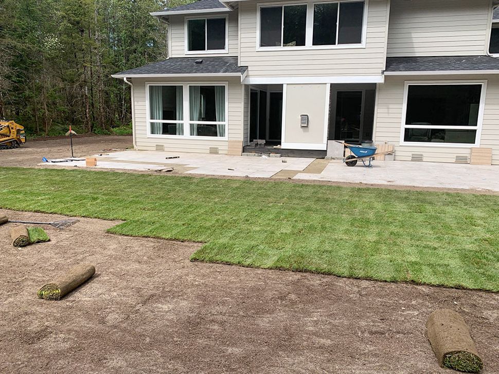 Laying sod in front of a two-story beige house. Rolls of sod on the ground.