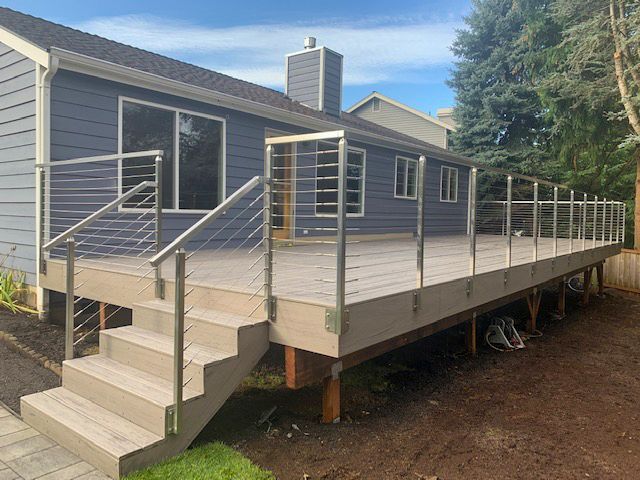 Wooden deck with stainless steel railings, stairs leading to it, built onto the back of a blue house.