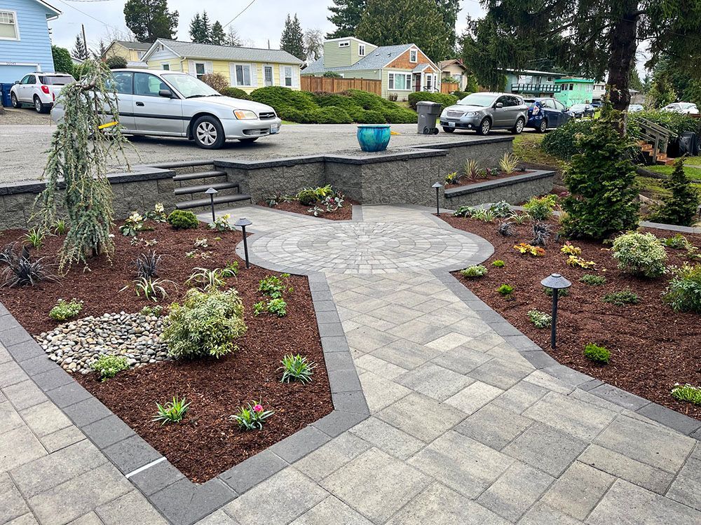 Paver walkway and garden with retaining wall leading to a house.