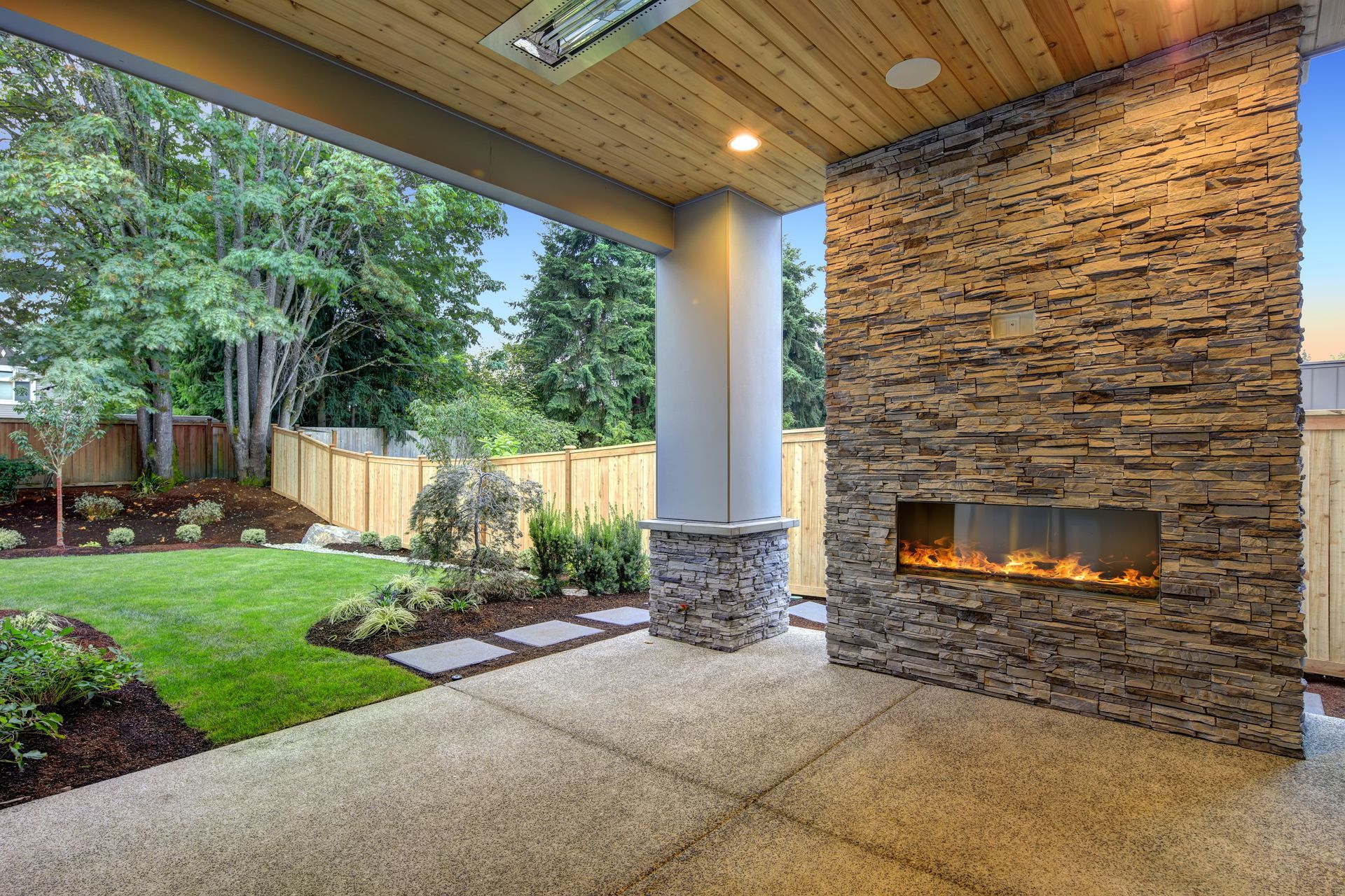 Outdoor patio with a stone fireplace, concrete floor, and a view of a green lawn.