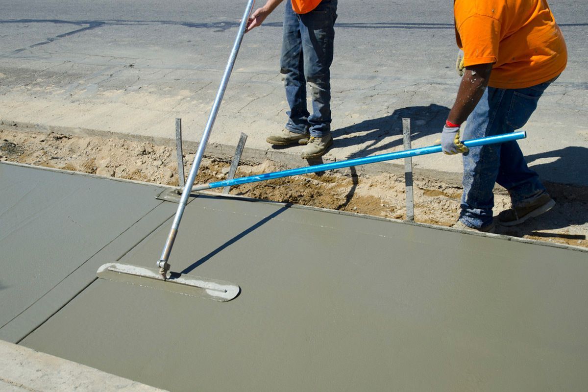A construction worker wearing orange gloves is pouring concrete on a construction site.
