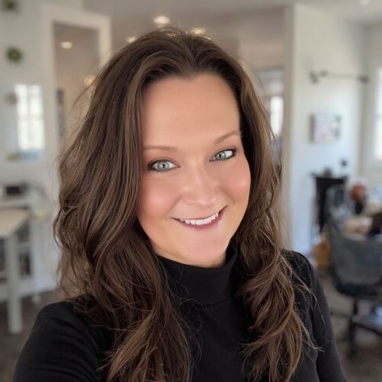 A woman is sitting at a desk with a laptop and a vase of flowers.