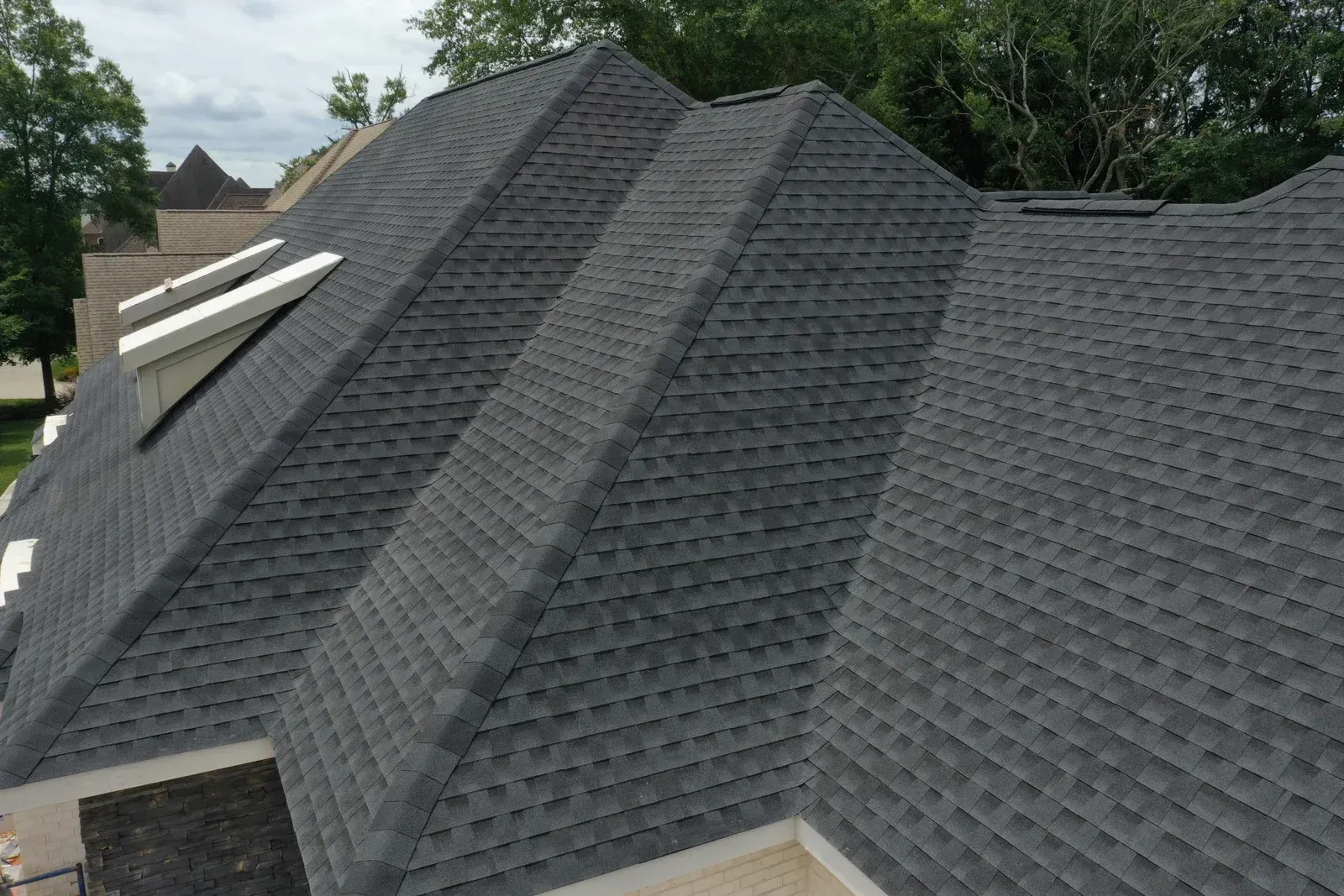 Dark gray asphalt shingle roof on a house with skylights, viewed from above, overcast sky.