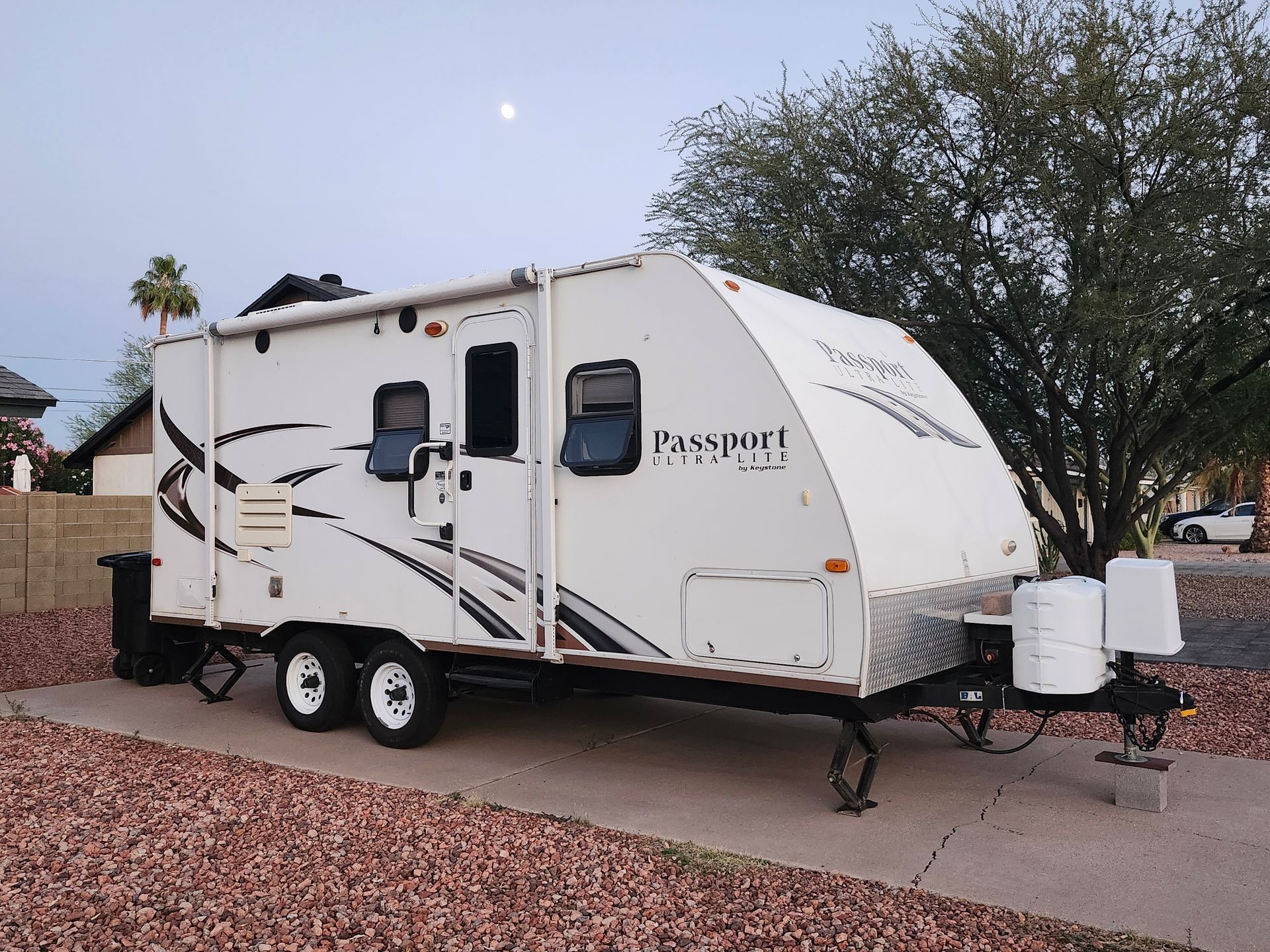 White travel trailer parked on a concrete pad with the moon in the background.