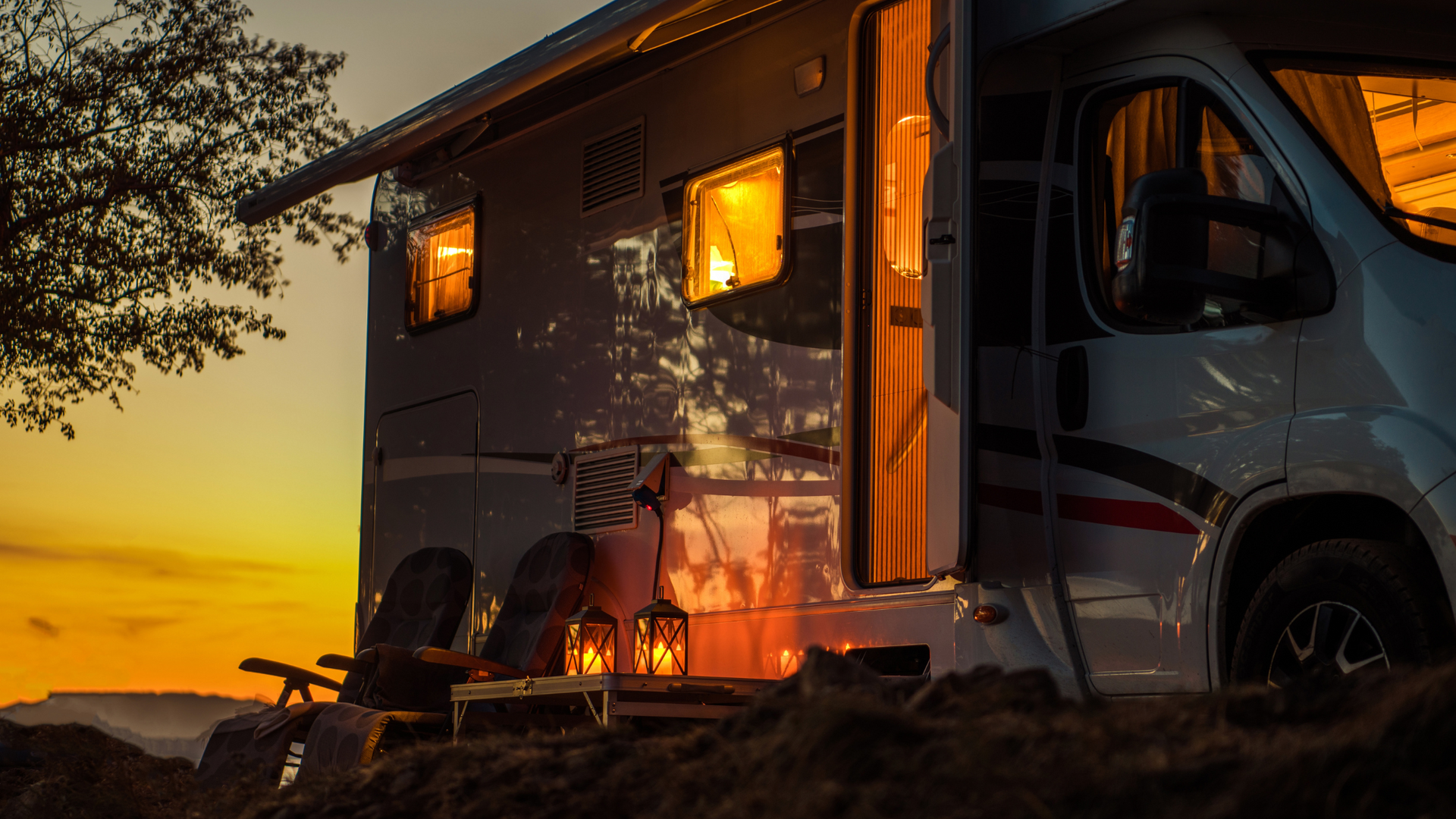A campervan parked at dusk, with open door, lit windows, and lanterns, set against an orange sky.