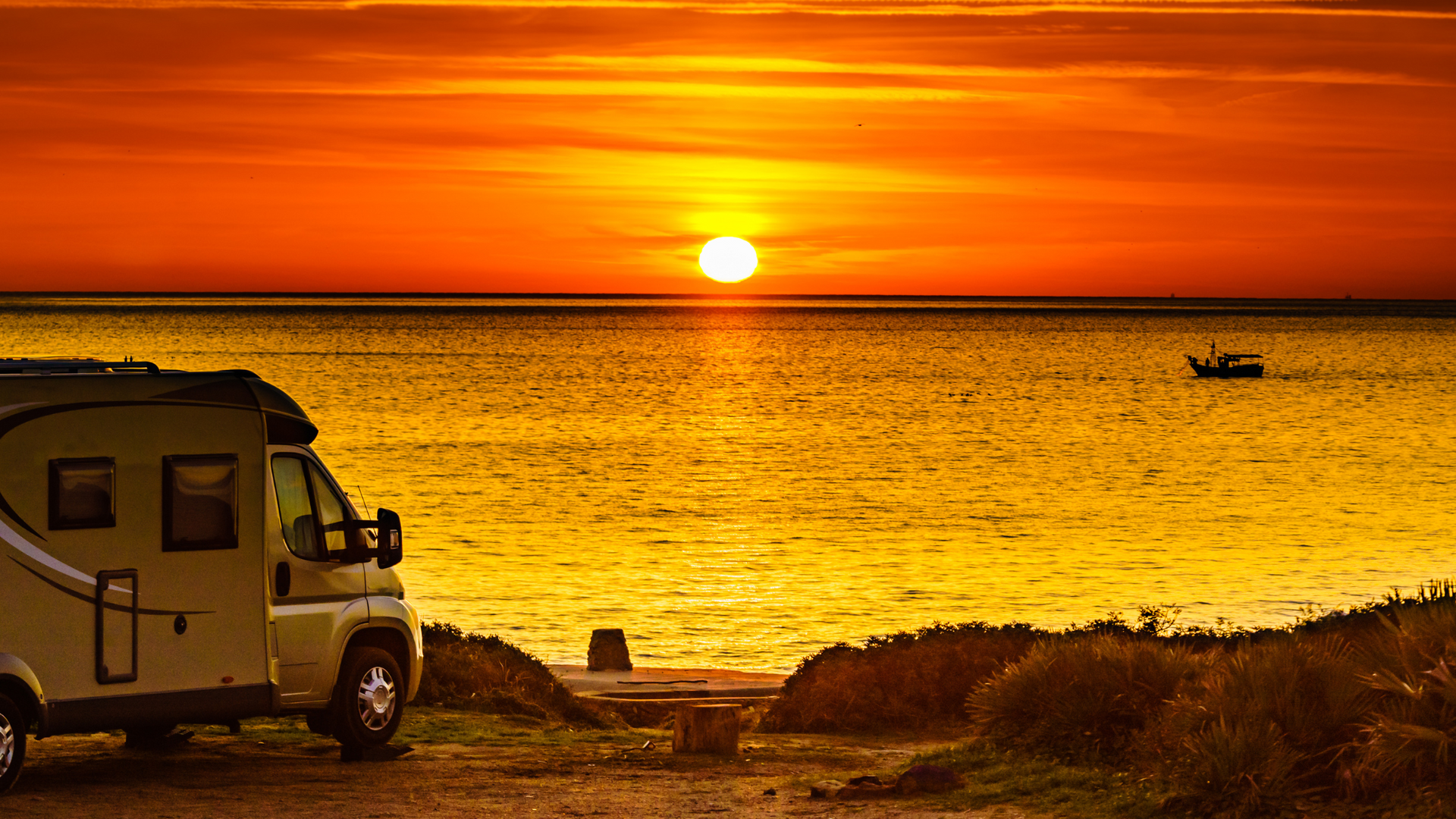 RV parked on beach at sunset, golden light reflecting on the ocean.