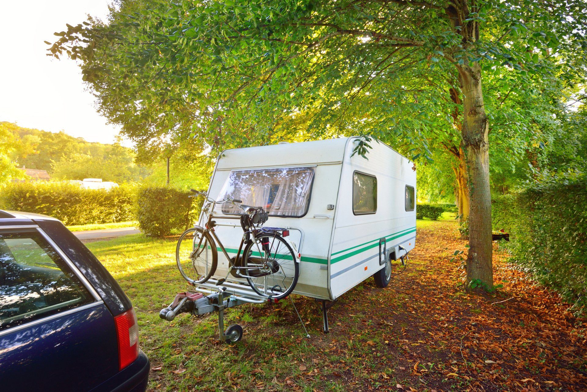 A camper with a bike attached to it is parked next to a car.