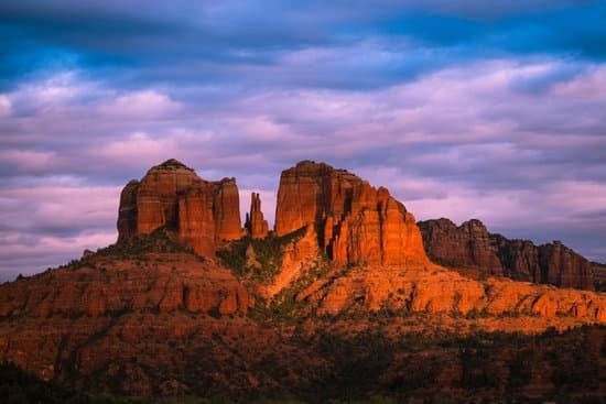 Red rock formations bathed in warm light, against a cloudy sky with shades of purple and blue, in Sedona, Arizona.
