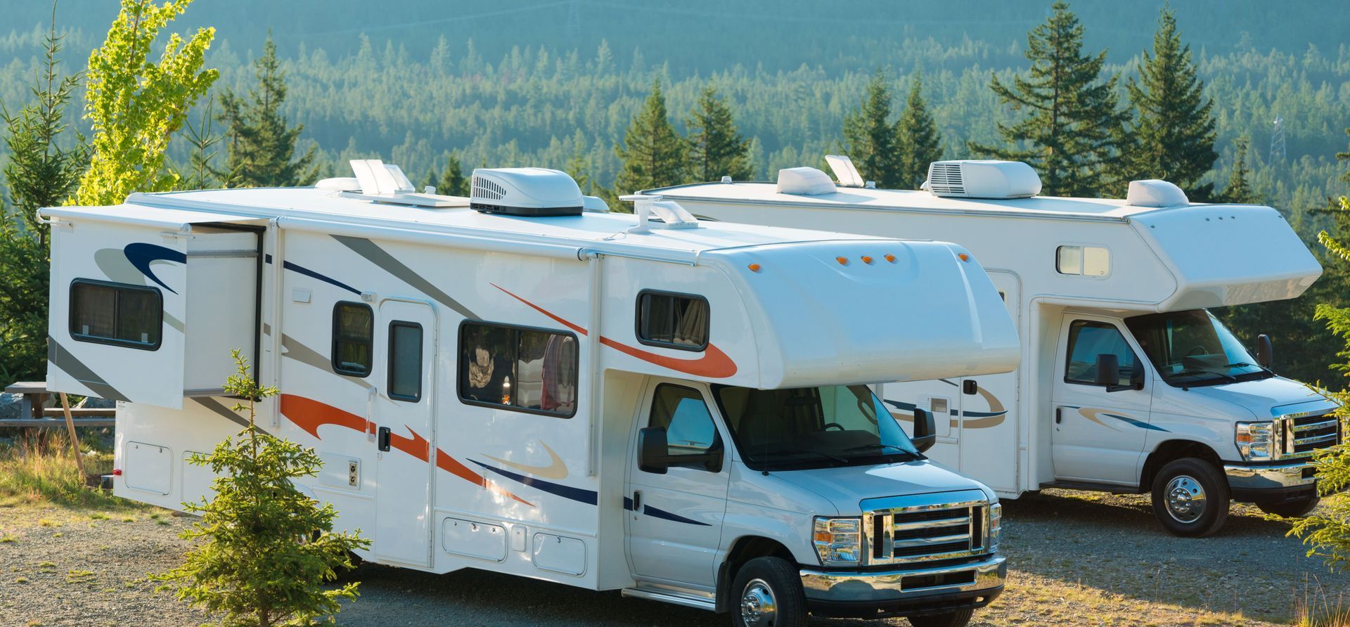 Two white rvs are parked next to each other on a gravel road.
