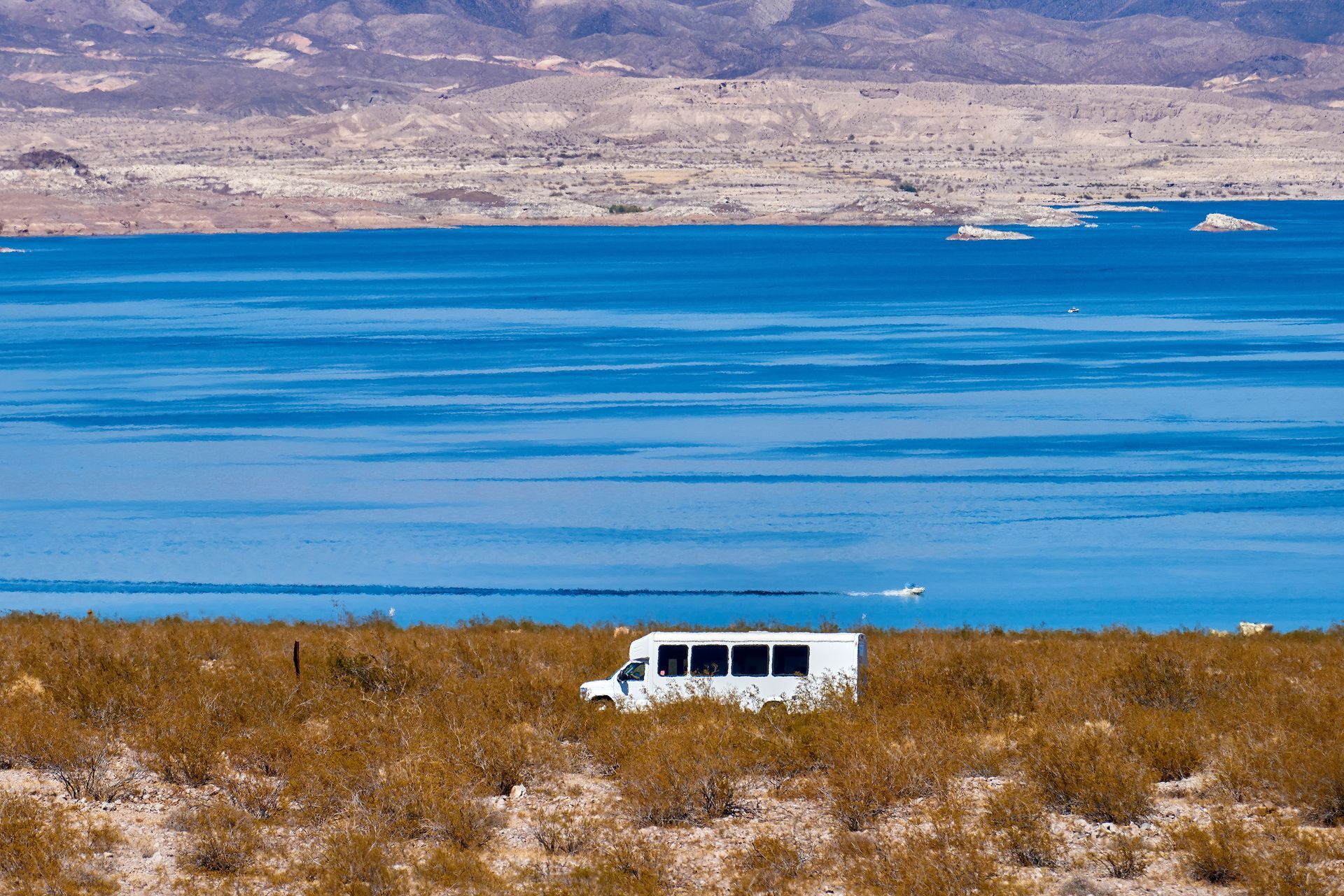 A white van is parked in the middle of a desert near a lake.